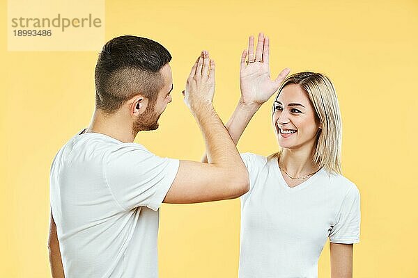 Junges lächelndes Paar  das sich gegenseitig high five gibt  auf gelbem Studiohintergrund. Mann und Frau spielen Flammkuchen