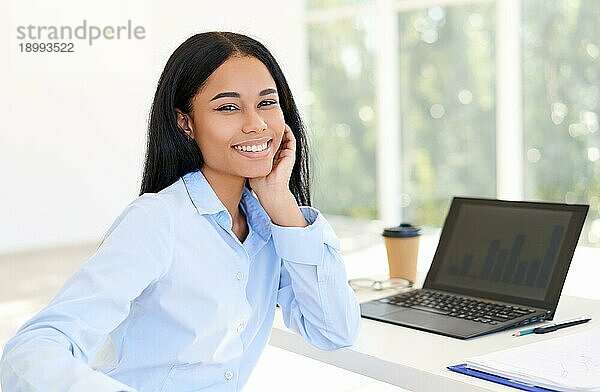 Glückliche schwarze Geschäftsfrau posiert an ihrem Schreibtisch in einem hellen modernen Büro