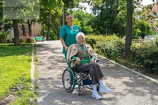 Porträt einer älteren Frau mit der Krankenschwester bei einem Spaziergang im Garten eines Pflegeheims im Rollstuhl