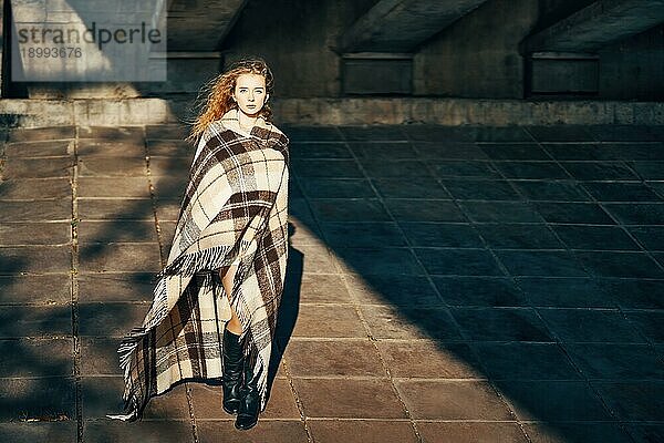 In voller Länge Porträt der hübschen jungen Frau in Decke eingewickelt posiert ib Sonne Lichter über städtischen Hintergrund. Expression  weibliche Schönheit  entspannen  Komfort Konzept