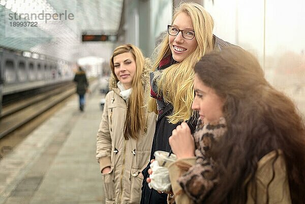 Attraktive junge Frauen unterschiedlicher Größe warten auf dem Bahnsteig eines modernen Pendlerbahnhofs im Freien auf einen Zug