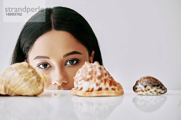 Schöne afroamerikanische Frau  die auf verschiedene Muscheln auf weißem Hintergrund schaut. Schönheit weiblich Konzept