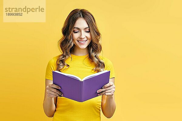 Lächelnde positive Mädchen lesen Buch auf gelbem Hintergrund. Hobby  Bildung Konzept