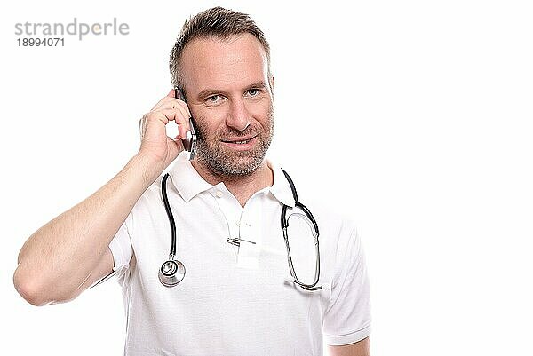 Männlicher Arzt mittleren Alters in weißem Hemd und Stethoskop  der mit einem zufriedenen Lächeln einen Anruf auf seinem Mobiltelefon entgegennimmt  während er dem Gespräch zuhört  vor weißem Hintergrund