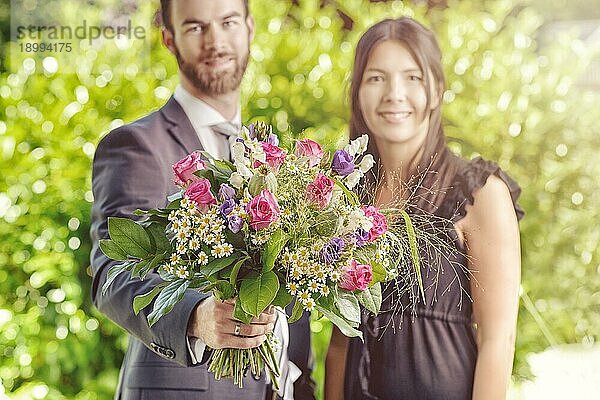Glückliches junges Paar im Garten mit einem Strauß verschiedener frischer Blumen  lächelt in die Kamera