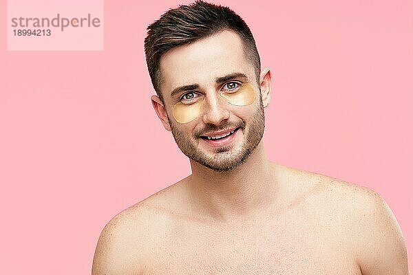 Porträt eines lächelnden gut aussehenden Mannes mit goldenen Augenklappen auf rosa Hintergrund. Männer Schönheit  Hautpflege Konzept