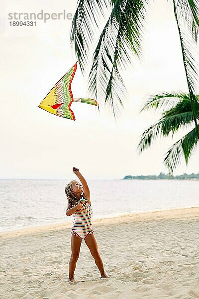 Glückliches kleines Mädchen mit fliegendem Drachen am tropischen Strand unter Palmen. Strand Spaß  glückliche Kindheit Konzept
