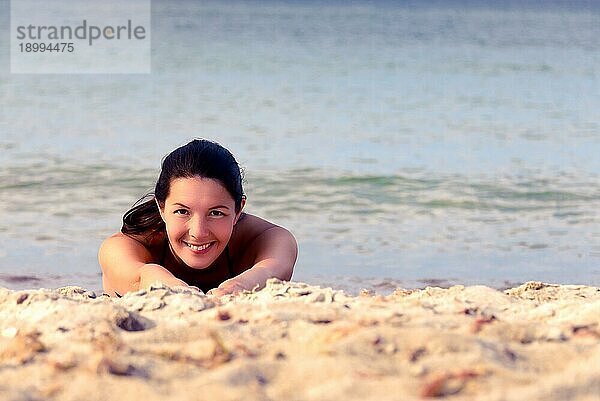 Glücklich lächelnde schöne junge Frau  die auf einer kleinen Welle am Meer surft  während sie einen tropischen Sommerurlaub am Strand genießt