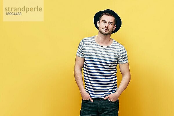 Modeporträt eines jungen Hipster Mannes mit Hut auf gelbem Hintergrund mit Kopierraum
