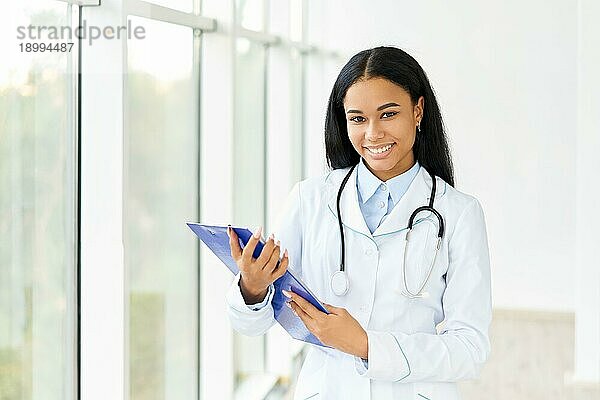 Glücklich lächelnder afroamerikanischer Arzt mit Klemmbrett im Krankenhaus. Medizin  Beruf und Gesundheitswesen Konzept