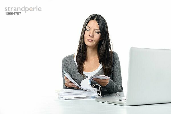 Serious Young Attractive Woman Scanning eine Mappe während der Forschung an ihrem Laptopcomputer auf dem Schreibtisch. vor weißem Hintergrund