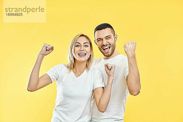 Glückliches Paar feiert den Erfolg mit Gewinner Geste auf gelbem Hintergrund. Sieg  Triumph und Emotionen Konzept