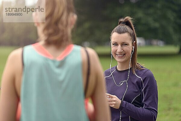 Halbkörperaufnahme einer gesunden jungen Frau mit Kopfhörern  die in die Kamera lächelt  während sie sich nach einer Outdoor Übung mit ihrem Smartphone in der Hand ausruht