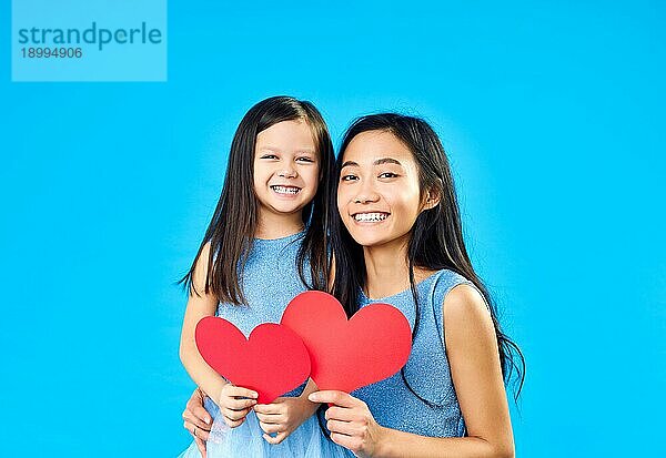 Lächelndes kleines Mädchen und ihre Mutter hält Papier Herz auf blauem Hintergrund. Glückliche Familie Liebe Konzept