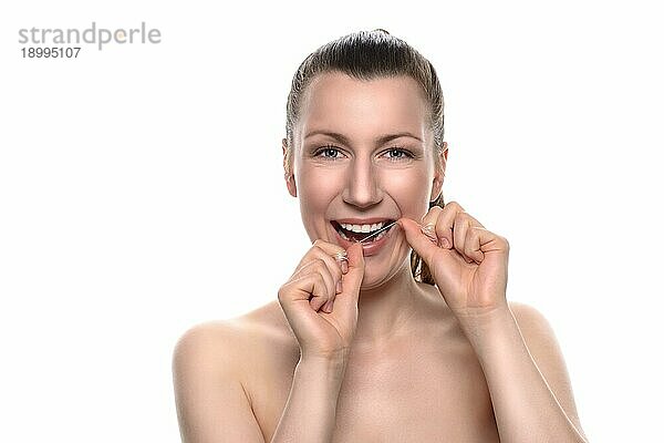 Lächelnde attraktive nackte Frau mit einem zahnigen Lächeln  die Zahnseide zwischen ihren Händen benutzt  in einem Konzept für Zahnpflege und Mundhygiene  vor weißem Hintergrund