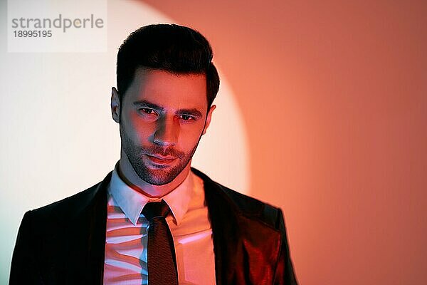Handsome trendigen Mann posiert im Rampenlicht auf Studio Hintergrund. noir Film Stil. Männer Schönheit Konzept