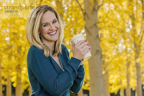 Ein schönes blondes Modell trinkt ein heißes Getränk  während es im Freien in einem Feld mit gelben Blättern posiert