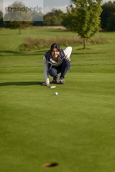 Eine Golferin  die einen Putt ausführt  kniet auf dem Grün und schaut auf das Loch  um das Gras und die eventuelle Wölbung eines Hangs zu prüfen