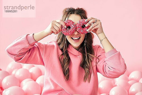 Lächelnde schöne Frau hat Spaß mit Donuts. Mädchen zeigt Donuts vor ihren Augen über rosa Hintergrund. Leckeres Essen  Diätkonzept