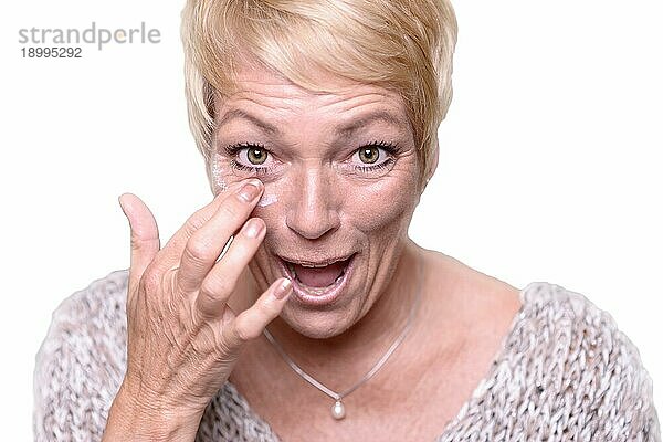 Attraktive blonde Frau mittleren Alters  die Anti Aging Creme auf die Falten um ihre Augen aufträgt  um das Altern in einem Hautpflege und Schönheitskonzept zu bekämpfen