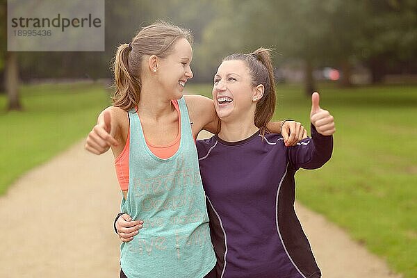 Halbkörperaufnahme von zwei glücklichen  gesunden Frauen im Park  die nach ihrem Training Daumen nach oben in die Kamera halten