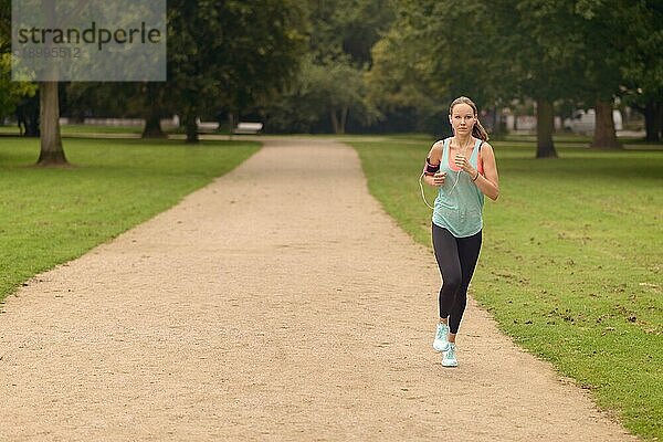 Ganzkörperaufnahme einer sportlichen Frau bei einer Laufübung im Park mit ernstem Gesichtsausdruck