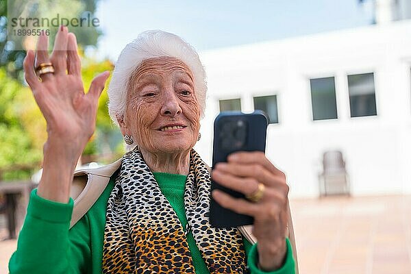 Ein älterer Mann im Garten eines Pflegeheims oder Seniorenheims an einem sonnigen Sommertag  der auf das Telefon schaut  Technologien im Alter