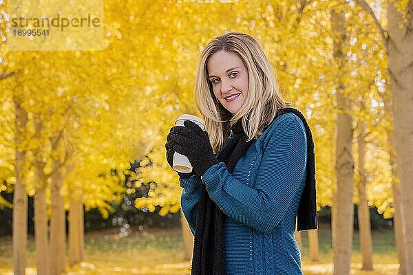 Ein schönes blondes Modell trinkt ein heißes Getränk  während es im Freien in einem Feld mit gelben Blättern posiert