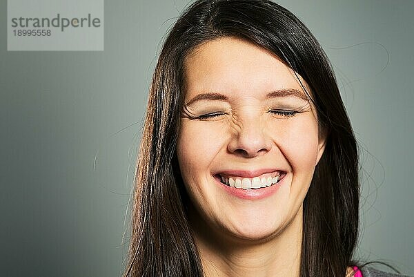 Glückliche  zufriedene Frau mit einem strahlenden Lächeln und geschlossenen Augen  Gesichtsporträt in Nahaufnahme auf grauem Studiohintergrund