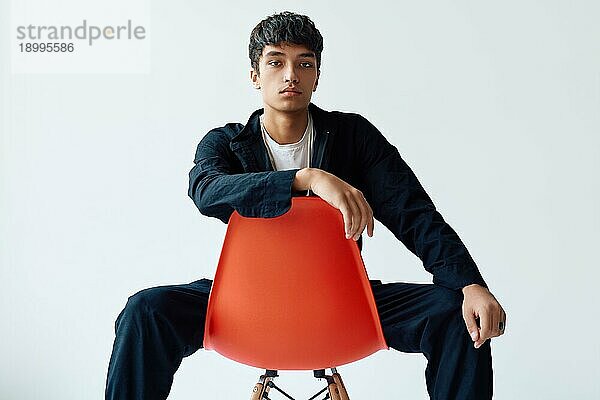Stylish gut aussehend junger Mann posiert auf Studio sitzt auf einem Stuhl Blick in die Kamera auf weißem Hintergrund. Mann Schönheit Konzept