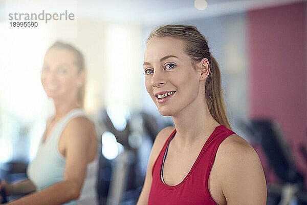 Attraktive junge Frau steht auf dem Laufband im Fitnessstudio  schaut in die Kamera und lächelt mit Kopie Raum