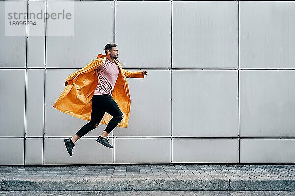 Trendy junger Mann in gelben Regenmantel Springen in der Luft auf Wall Street städtischen Hintergrund. sorglos  Freiheit  Flucht Konzept