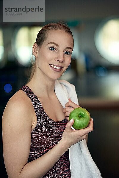 Attraktive  natürliche  junge Sportlerin  die einen frischen  knackigen  grünen Apfel in der Hand hält und mit einem ruhigen Lächeln in die Kamera blickt  in einem Konzept für gesunde Ernährung