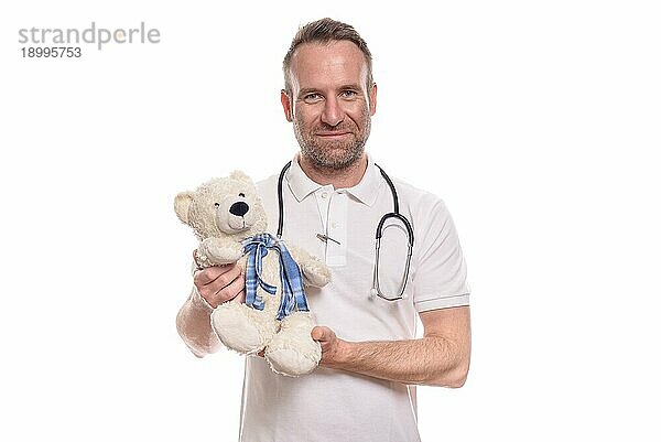 Lächelnde Kinderärztin oder männlicher Kinderkrankenpfleger  die der einen niedlichen  ausgestopften Teddybären hält  während er versucht  einen jungen Patienten auf der Krankenhausstation zu trösten und zu beruhigen  vor weißem Hintergrund
