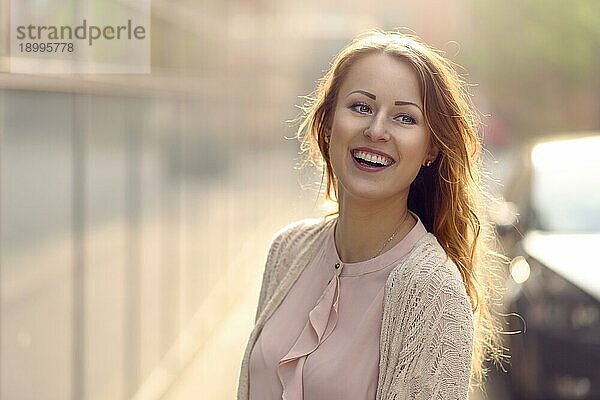 Fröhliche junge Frau  die in die Kamera lacht  in der frühen Morgensonne im Freien mit Kopierraum links