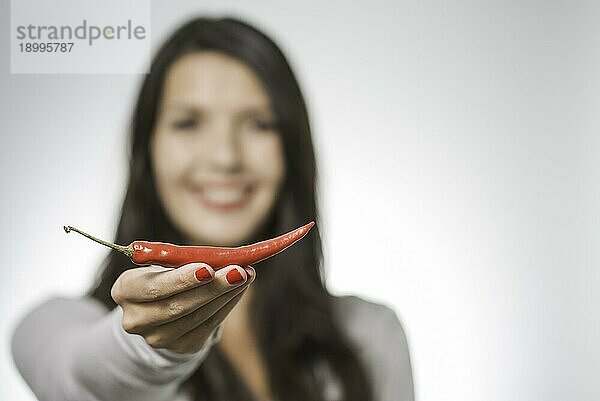Frau  die eine rote  scharfe Chilischote oder getrockneten Cayennepfeffer in der Hand hält  der in der Küche als scharfes  aromatisches Gewürz verwendet wird  mit selektivem Fokus