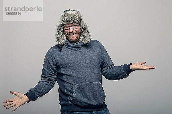 Fröhlicher Mann mit Brille und Wintermütze  jubelnd und feiernd  über grauem Hintergrund mit Leerzeichen