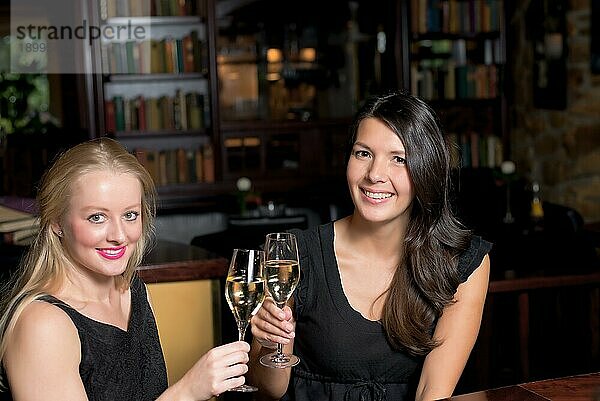 Zwei schöne elegante Frauen Freunde in stilvollen einfachen schwarzen Cocktailkleider Toast einander mit Gläsern von gekühlten Champagner  wie sie auf eine Nacht zusammen feiern