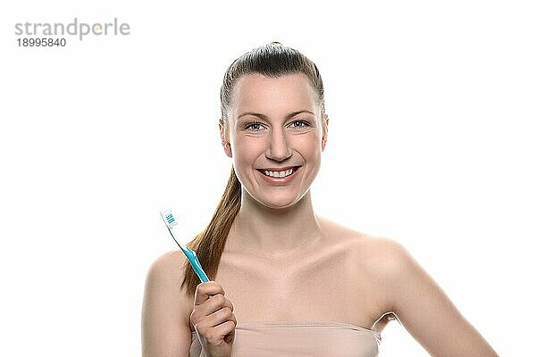 Lächelnde gesunde Frau mit nackter Schulter und einem freundlichen Lächeln  die eine Zahnbürste in der Hand hält  Konzept der Zahnmedizin  Mundhygiene und Kariesprävention  vor weißem Hintergrund
