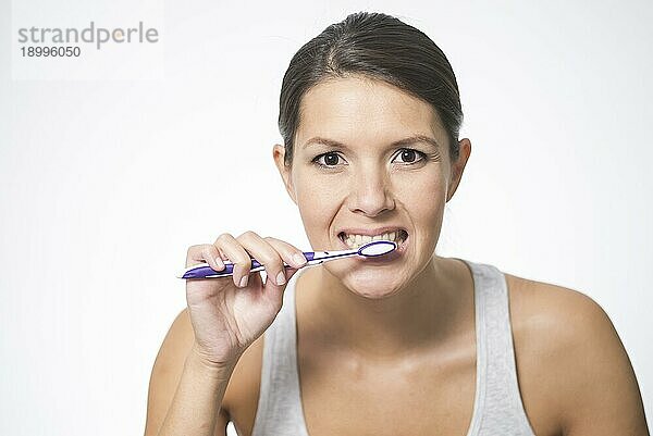 Attraktive Frau bei der Zahnpflege  die sich mit Zahnbürste und Zahnpasta die Zähne putzt  um Karies vorzubeugen  vor weißem Hintergrund