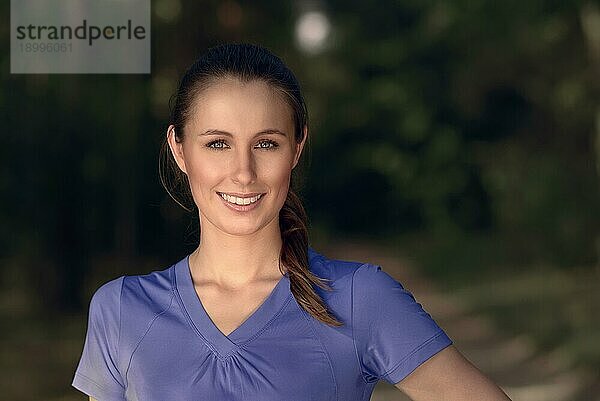 Lächelnde attraktive junge Frau im blaün TShirt die im Freien in der Dunkelheit steht und in die Kamera schaut  mit Kopiervorlage