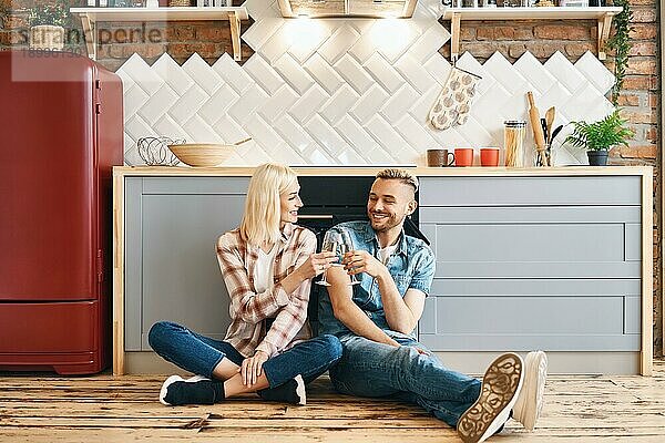 Romantische glückliches Paar sitzt auf dem Boden in der Küche und Toasting Champagner Gläser. Beziehung  Feier  Dating Konzept