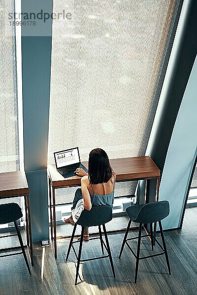 Draufsicht auf eine junge schöne Frau  die an einem Laptop in einem modernen Büro oder Café arbeitet