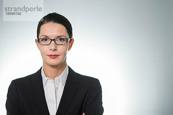 Stilvolle  selbstbewusste Geschäftsfrau mit Brille  die mit verschränkten Armen und ernstem Gesichtsausdruck direkt in die Kamera schaut  Porträt einer Führungskraft oder Managerin mit Kopierbereich