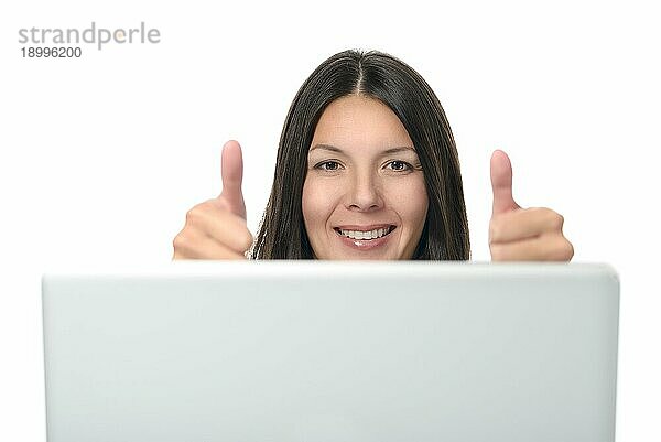 Attraktive Frau zeigt Daumen hoch Zeichen auf beiden Händen vor einem Computergerät. vor weißem Hintergrund