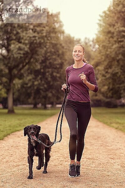 Totale Aufnahme einer gesunden jungen Frau beim Joggen im Park mit ihrem schwarzen Hund