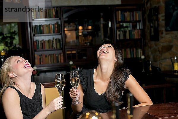 Zwei elegante Frauen  die Champagner trinken und feiern  sitzen an einem Tisch in einem gehobenen Hotel  Restaurant oder Nachtclub und amüsieren sich prächtig  mit Copyspace