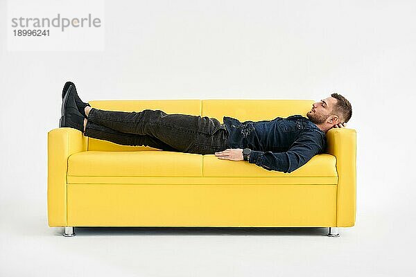 Junger Mann entspannt allein auf gelbem Sofa zu Hause. Ruhe Konzept