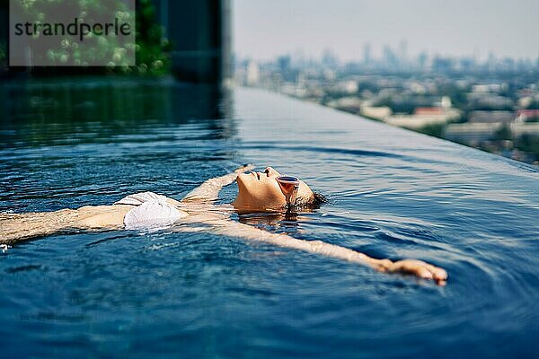 Junge Frau entspannt sich im Schwimmbad auf dem Dach und schwimmt im Wasser. Sommerurlaub Konzept