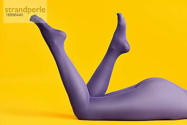 Schlanke Beine der schönen jungen Frau in hellen lila Strumpfhosen entspannen auf gelbem Hintergrund. Rest Konzept  weibliche Schönheit